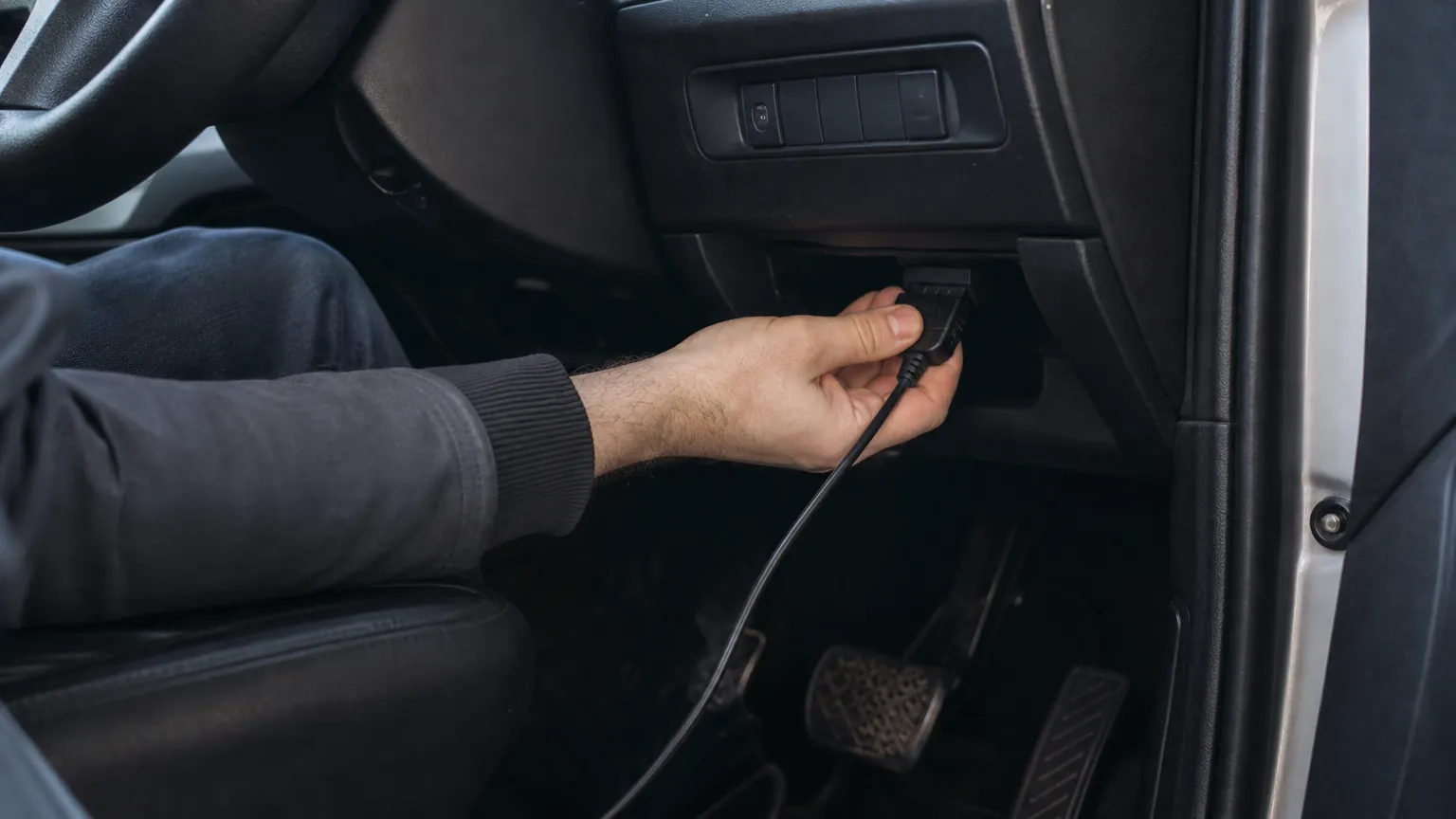 Hands plugging a small adapter into a port under a dashboard